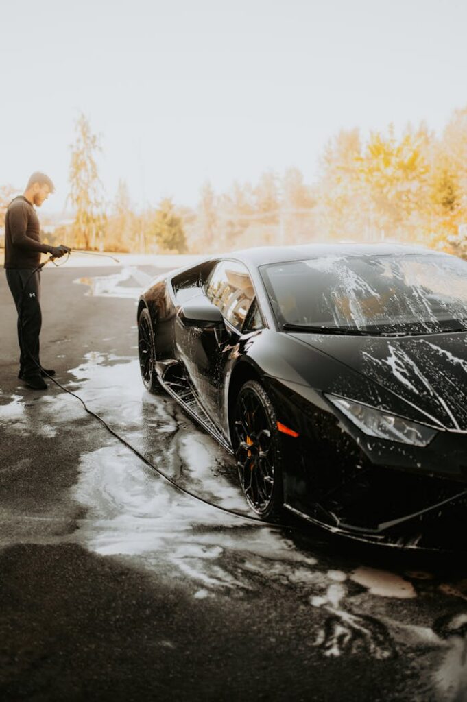 A man washing a sleek black Lamborghini sports car with soap suds outdoors.